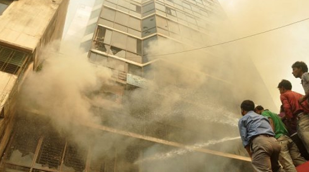 Onlookers watch as firefighters try to control a garment factory fire in Bangladesh, on November 26, 2012/AFP