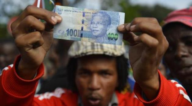 A man holds a 100 rand bill bearing the portrait of South African former president Nelson MandelaMandela as Mandela's funeral cortege drives through the streets in Pretoria on December 11, 2013/AFP