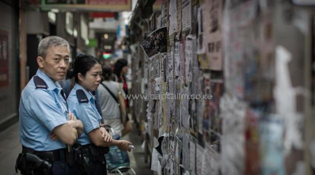 Members of the police look at pro-democracy posters displayed on a bus stop near the encampment of a protest site in the Mongkok district of Hong Kong on November 12, 2014/AFP