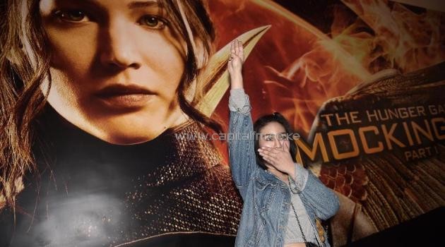 A Thai student flashes a three-finger salute -- a symbol of resistance against the army's May coup -- as she stands beside a poster for the latest Hunger Games film at a cinema in Bangkok, on November 20, 2014/AFP