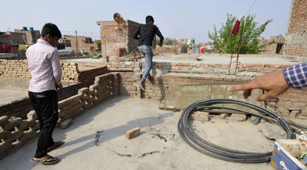 Young men point out the spot on a roof where a teenage girl was found after being allegedly raped and then set on fire in Greater Noida, India/AFP
