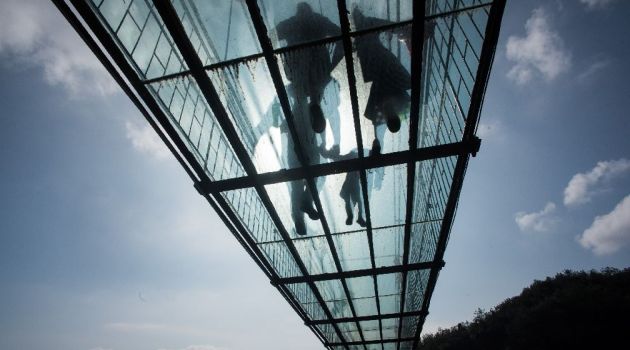 Chinese tourists walk across a glass-bottomed suspension bridge in the Shiniuzhai mountains in Hunan province on October 8, 2015/AFP
