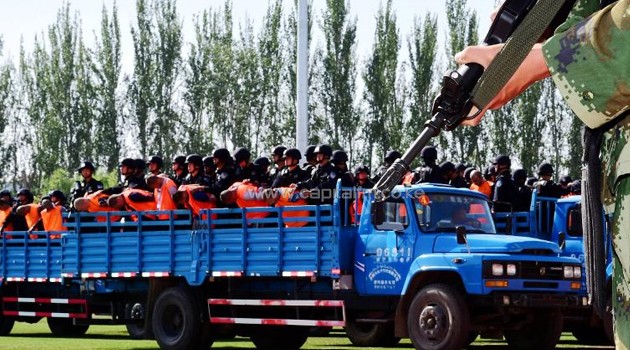 Security forces stand behing the accused (in orange vests) on trucks, during a mass sentencing in Ili prefecture, northwest China's Xinjiang region, on May 27, 2014/AFP