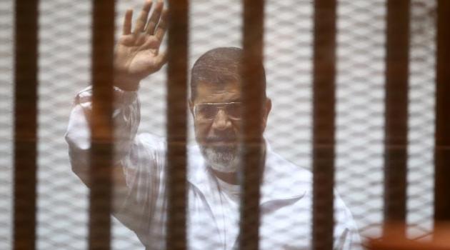 Egypt's deposed Islamist president Mohamed Morsi waves inside the defendants cage during a trial at the police academy in Cairo on December 7, 2014/AFP