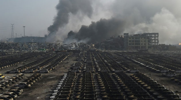 Smoke billows behind rows of burnt-out cars at the site of a series of explosions in Tianjin, northern China, on August 13, 2015/AFP