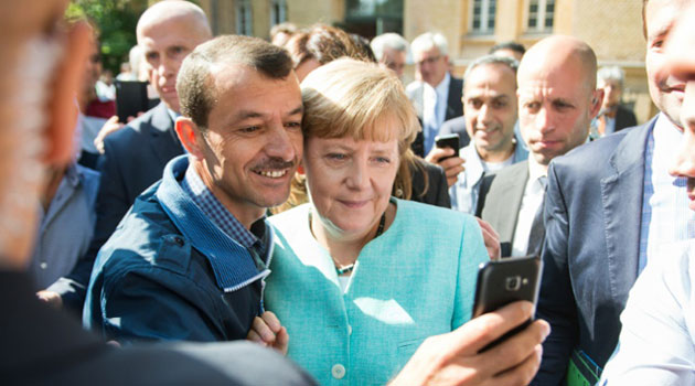 An asylum-seeker takes a "selfie" with German Chancellor Angela Merkel during her visit to a refugee camp in Berlin on September 10, 2015/AFP