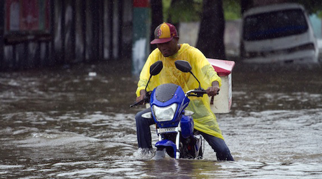 A local resident drives a bike in a flooded street caused by a storm/AFP