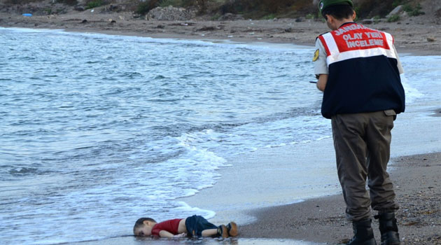 A Turkish police officer stands next to the body of a migrant child on the shores in Bodrum, southern Turkey, on September 2, 2015 after a boat carrying refugees sank while trying to reach the Greek island of Kos © Dogan News Agency/AFP