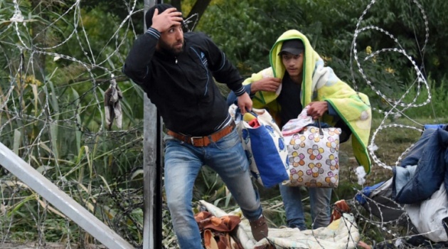 People cross through a hole in a barbed-wire fence at the Hungarian-Serbian border near Roszke, on September 10, 2015/AFP  