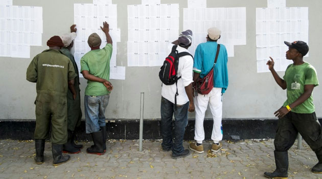 Men look for their names on lists outside a polling station in Dar es Salaam on October 24, 2015/AFP