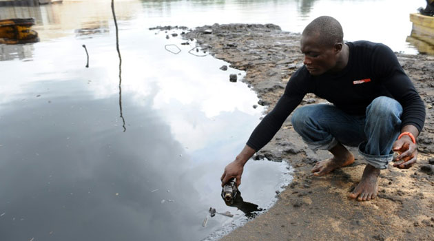 A man scoops spilled crude oil into a bottle from the waters of the Niger Delta swamps of Bodo, a village in Ogoniland, on June 24, 2010  © AFP/File