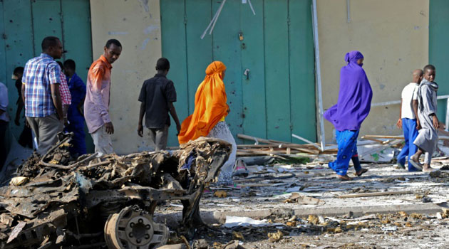 People walk past the wreckage of a car after a bomb blast in Mogadishu on December 19, 2015/AFP