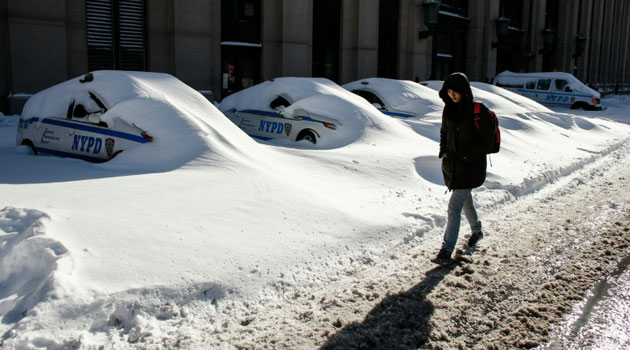 A woman walks past police cars covered in snow in New York on January 24, 2016/AFP