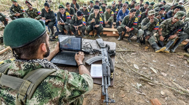 With the sun beating down on him Tomas (L), a member of the Revolutionary Armed Forces of Colombia (FARC), sits by his laptop computer and explains the issues covered by the peace talks/AFP