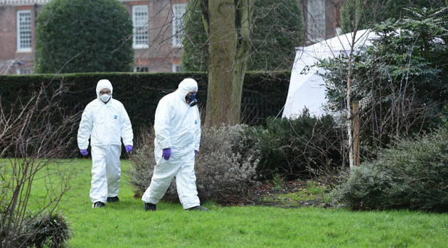 Forensics officers in overalls and masks walk past a tent erected over the spot where a man died after being discovered on fire in the park outside the wall of Kensington Palace, central London on February 9, 2016/AFP