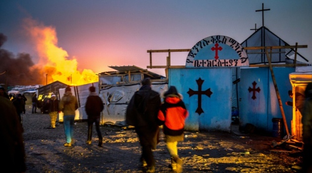 Migrants walk past a church towards burning shacks in the southern part of the so-called "Jungle" migrant camp in the French port city of Calais/AFP Philippe Huguen