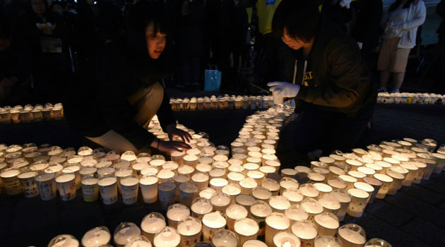 High school students light candles to remember victims of Japan's 2011 tsunami on March 11, 2016/AFP