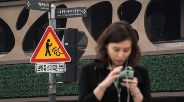 A sign advising pedestrians of the dangers of using smartphones while walking is displayed at an intersection in central Seoul on June 22, 2016/AFP)