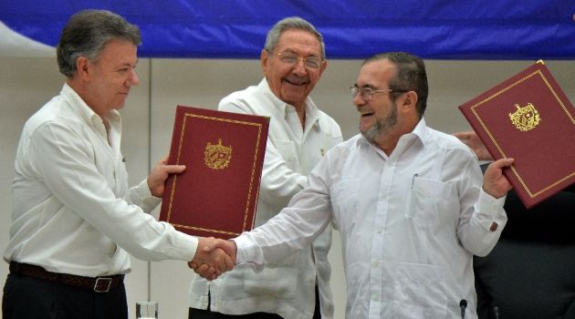 Colombia's President Juan Manuel Santos and Timoleon Jimenez, head of the FARC, shake hands accompanied by Cuban President Raul Castro during the signing of the peace agreement in Havana on June 23, 2016/AFP