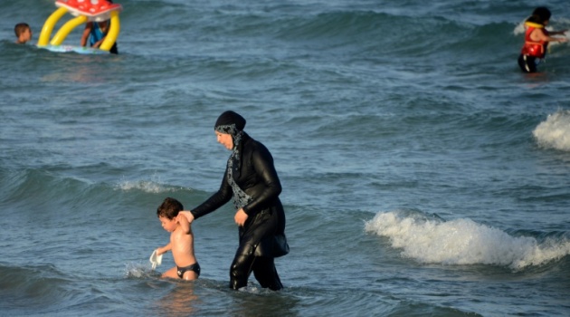 A Tunisian woman wearing a "burkini", a full-body swimsuit designed for Muslim women, walks in the water with a child on August 16, 2016 at Ghar El Melh beach near Bizerte, north-east of the capital Tunis/AFP  