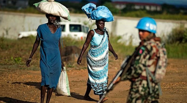Displaced women carry goods as a Nepalese peacekeeper patrols outside the premises of the UN Protection of Civilians (PoC) site in Juba/AFP
